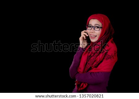 Portrait of young muslim woman holding on mobile phone on black background.Islamic fashion.