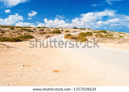 One round road sign with a number 30 near a winding asphalt road near Cape Greco, Cyprus. Many white clouds in the sky, barren orange sandy hill, vast expanse. Warm day in fall