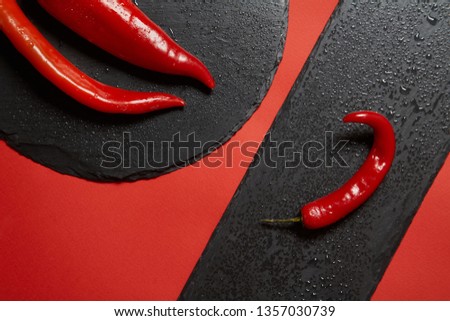 Red hot chili pepper and red peppper on a black slate dish on a red background.