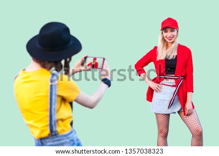 Capture the moment. Two stylish hipster girls in fashionable clothes having fun together, brunette woman making pictures of her best friend, positive friendship mood, photographer on work, Indoor