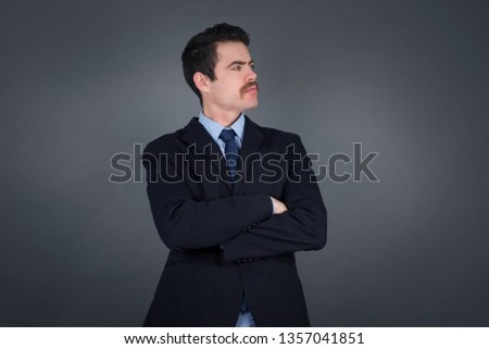 Image of upset pretty young caucasian businessman standing indoors with arms crossed. Looking with disappointed expression aside after listening to bad news. Confident man.
