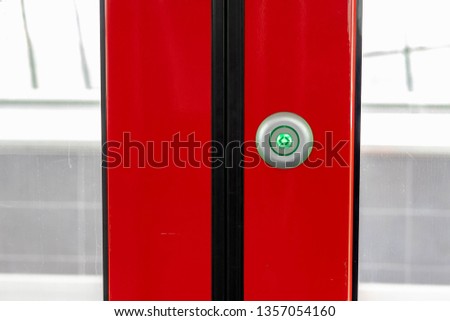 Red door of metro carriage with the button press to open sliding mechanical door at a train station platform.