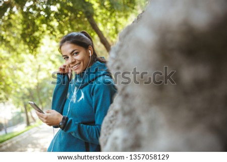 Close up of an attractive young fitness woman wearing sportswear exercising outdoors, listening to music with earphones