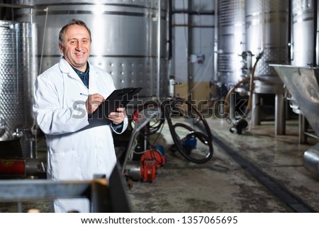 Diligent positive wine maker examines equipment at winery and writes down remarks Royalty-Free Stock Photo #1357065695