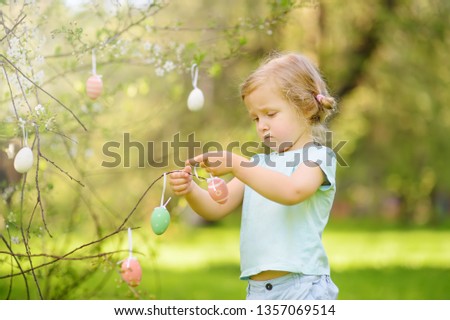 Cute little girl hunts for easter egg on branch flowering tree.Traditional easter festival outdoors.