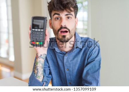 Young man holding dataphone point of sale as payment scared in shock with a surprise face, afraid and excited with fear expression