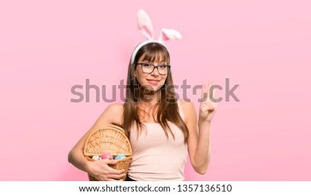Young woman wearing bunny ears for Easter holidays happy and counting four with fingers on pink background