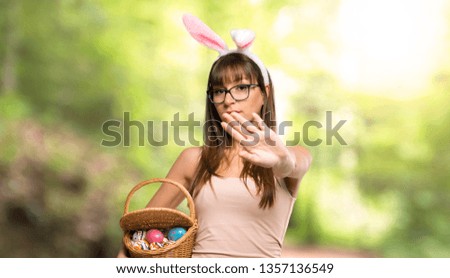 Young woman wearing bunny ears for Easter holidays making stop gesture with her hand denying a situation that thinks wrong at outdoors
