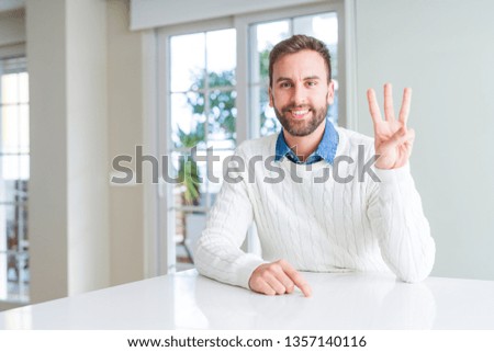 Handsome man wearing casual sweater showing and pointing up with fingers number three while smiling confident and happy.