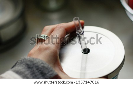 Hand holding a transparent straw of a stainless steel silver thermos. Travel coffee cup