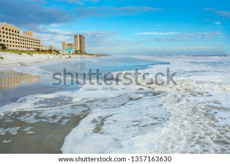 Ocean and beach landscape, cloudy blue sky and hotels and buildings in the background. Beautiful white sea foam on the beach. Jacksonville Florida, USA,