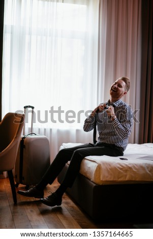 Man sitting on the bed and fixing his tie. Manager taking of his tie after working on the laptop. Guy taking a break from work.