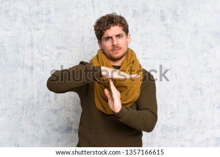 Blonde man over grunge wall making time out gesture