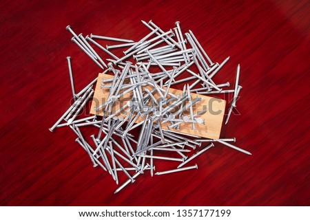 Seven nails stuck in a piece of wood and a group of nails around it, all on a wooden finish surface