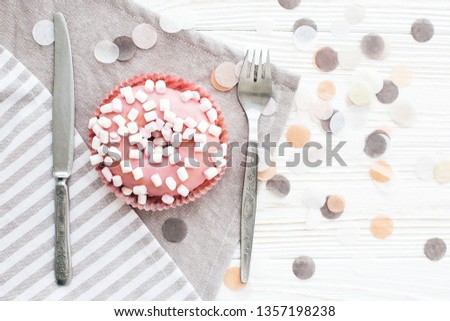 Delicious colorful pink donut with sprinkles and marshmallows on stylish white table with confetti and fork and knife, flat lay. Party concept. No diet. Candy bar at wedding reception.
