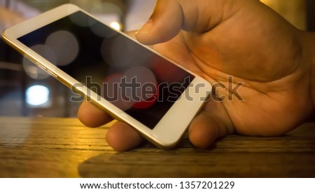 Hand holding the smartphone on the wooden table with bokeh lighting background 