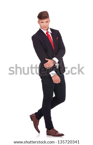 full length picture of a young business man posing with a serious expression on his figure while holding a hand with the other. isolated on white background