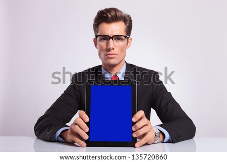 young business man sitting at the desk and showing you his tablet, on gray background