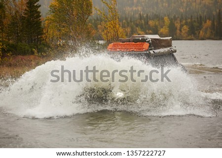 An SUV car is wade along a river, splashes are flying against the background of an autumn forest on a rainy day. Extreme and Dangerous Off Road Tourism