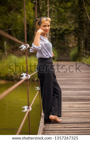 Women white skin lovely brown hair red lip wear Gray shirt with yellow glasses tuck collar wearing black pants women standing poses photography portrait on the bridge sling wooden floor.