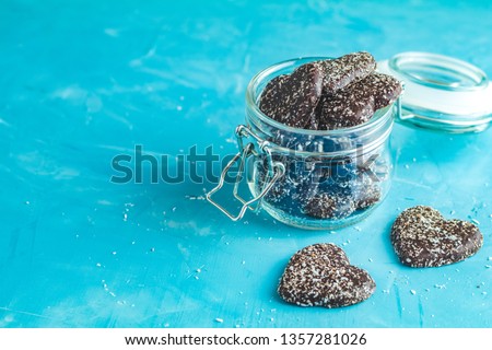 Delicious baked Heart shaped chocolate cookies with coconut chips in glass jar on blue concrete table surface. Food greeting card with copy space for you text.