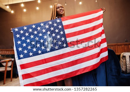 Beautiful african woman in stylish casual clothes posing with USA flag at hands in office.
