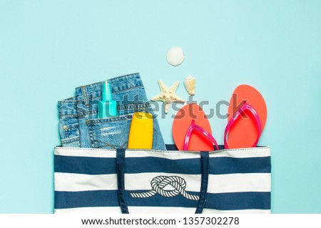 Summer sea accessories. Beach bag Coral flip flops denim shorts shells starfish sunscreen bottle body spray on blue background top view flat lay. Summer background. Holiday vacation travel concept.