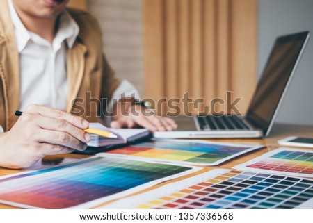 Creative graphic designer using graphics tablet to choosing color swatch samples chart for selection coloring with work tools and accessories while working with computer at studio.