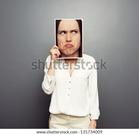 young woman covering image with big pensive face. concept photo over grey background
