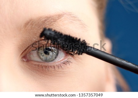 Female Slavic young girl portrait with gray-blue eye and light brown eyebrows close-up photo of half face doing eyelashes makeup with mascara, natural beauty