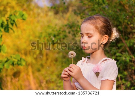 Beautiful little girl with dandelion blowing at summertime in nature outdoor