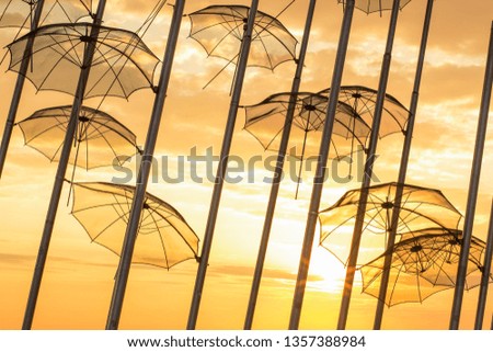 colorful bright picture of exterior landscaping object outdoor hanging street umbrellas on high pillars on vivid yellow and orange sunny light sky in sunset time background