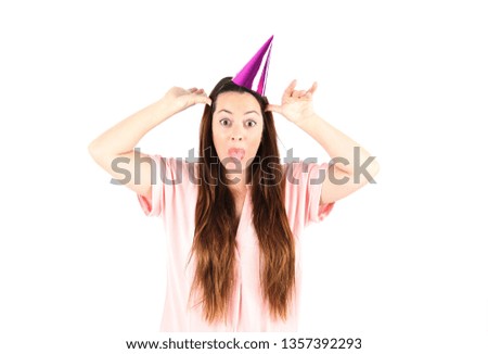 Confident young woman being funny while wearing a pink party hat against a white background