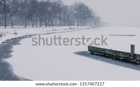 Frozen river and dock covered in snow with trees in the background.