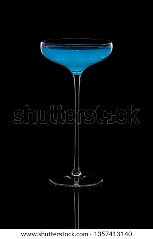 Cocktail based on carbonated drink in a beautiful glass on a thin long leg isolated on black with reflection.