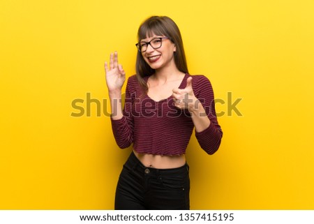 Woman with glasses over yellow wall showing ok sign with and giving a thumb up gesture