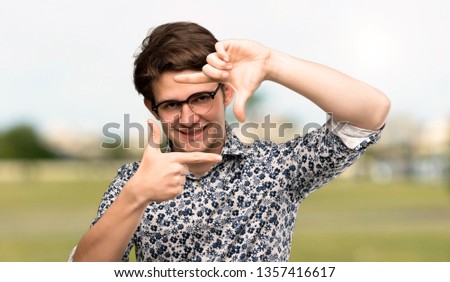 Teenager man with flower shirt and glasses focusing face. Framing symbol at outdoors
