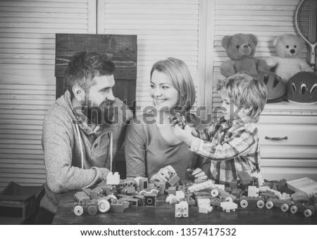 Construction games concept. Parents and kid with happy faces hold colorful bricks. Young family play game with construction blocks. Father, mother and son in playroom on light wooden background.