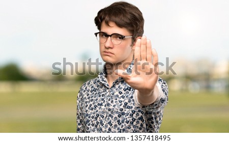 Teenager man with flower shirt and glasses making stop gesture denying a situation that thinks wrong at outdoors