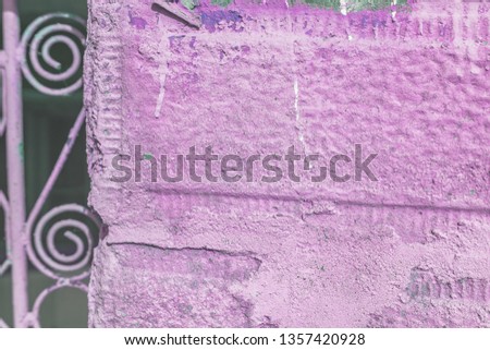 A close-up of a fragment of an old rural door. Stone fence painted in purple and metal door with ornaments. Shallow depth of focus, texture, background.
