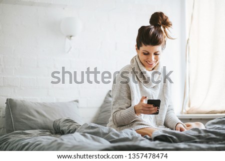 Portrait of a beautiful girl sitting on the bed while holding cellphone 