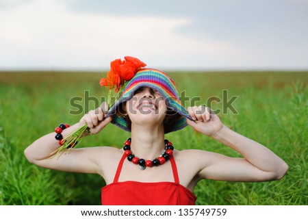 Young smiling pretty girl n a hat with poppies on a background of green field.
