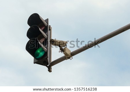 Outdoor surveillance camera and green traffic light both installed on a pole above a roadway, against a blue sky. Modern automatic traffic control. Copy space.