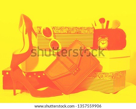 Flat lay female outfit layout: accessories shoes, handbag clutch, sunglasses, cosmetics makeup, alarm clock on carton boxes on red yellow background. Concept for online shopping, duotone.