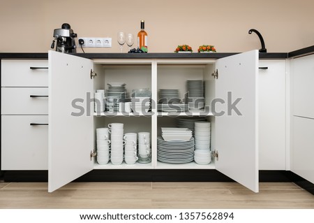 Dishware storage cabinet with open doors, white plates, bowls cups and other china crockery inside, front view Royalty-Free Stock Photo #1357562894