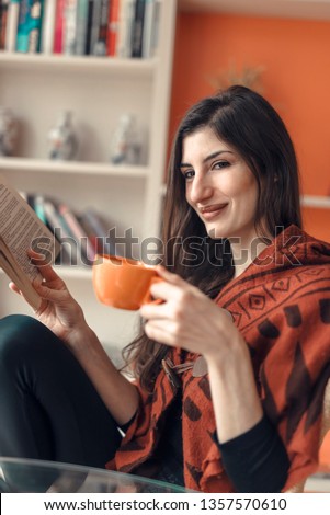 Young beautiful woman reading a book at home, enjoying a cup of coffee and good read
