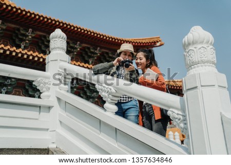 Friendship travel summer vacation concept. two asian female friends looking at photos in camera standing on white stone stairs with dragon pattern on it leaning railing in confucius temple beijing.