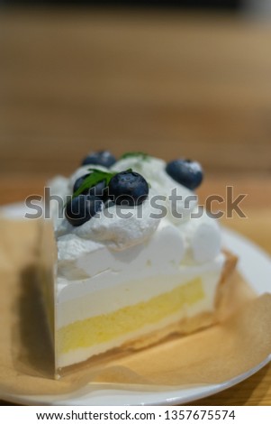 Delicious white-yellow cream cake on the plate decorated with fresh blueberries on top.