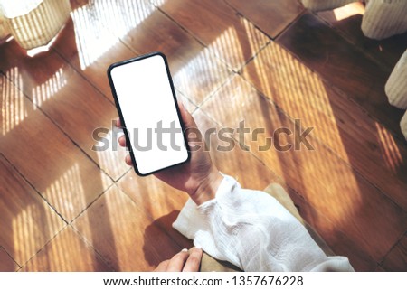 Top view mockup image of a woman holding and using black mobile phone with blank desktop screen while laying down on the floor with feeling relaxed