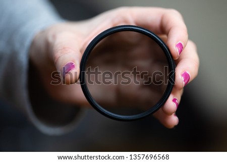 A young female hand with pink nail polish holds a neutral density (ND) filter for a digital SLR camera.